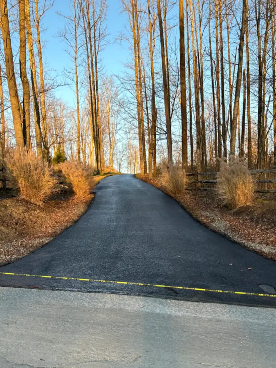 Freshly sealed Judah Paving driveway running back through tall fall woods past a board fence