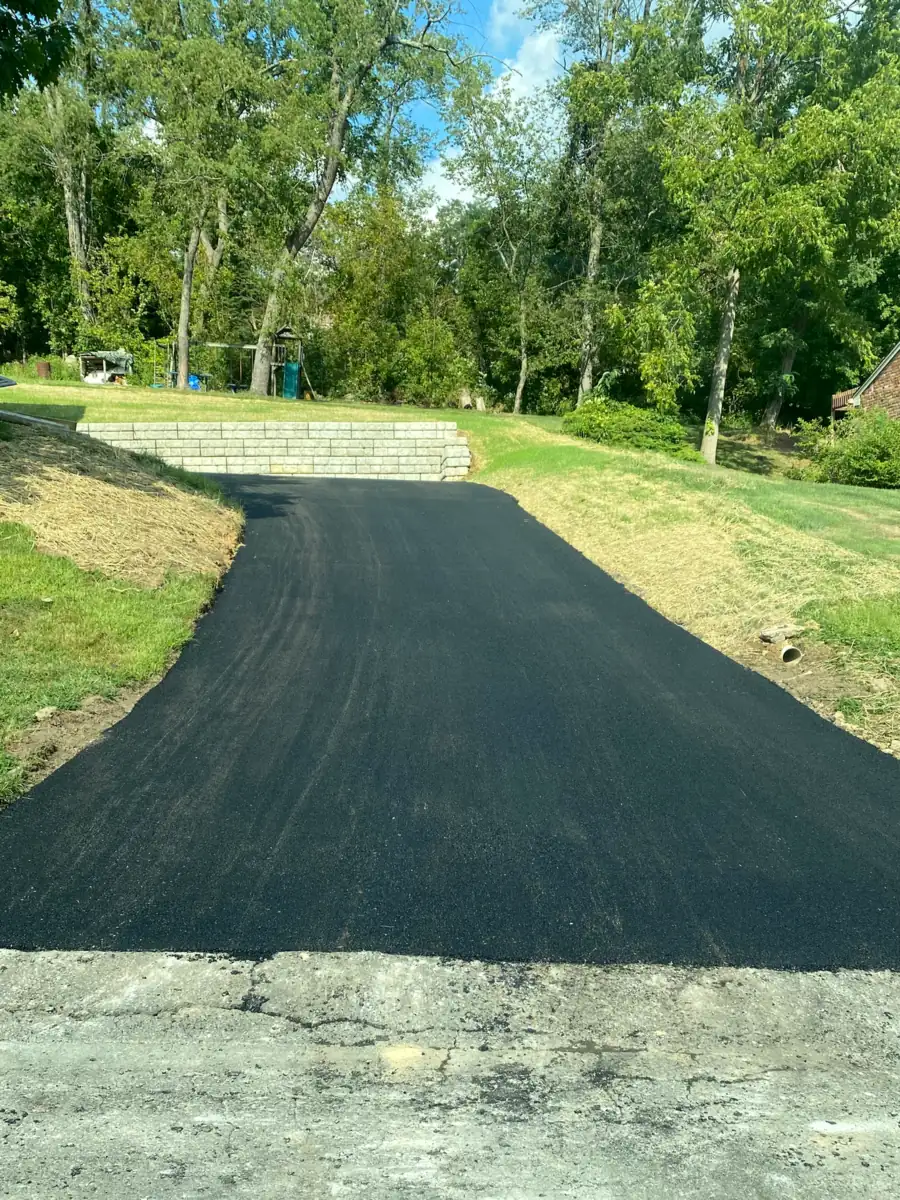 New asphalt driveway climbing a green yard where it meets an old broken concrete pad