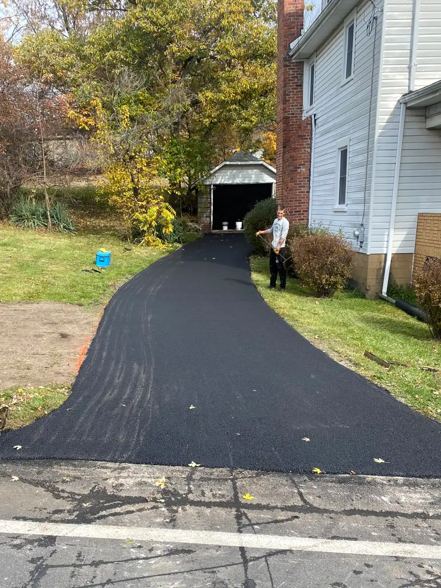 New asphalt driveway running back along a white house to a detached garage in the fall