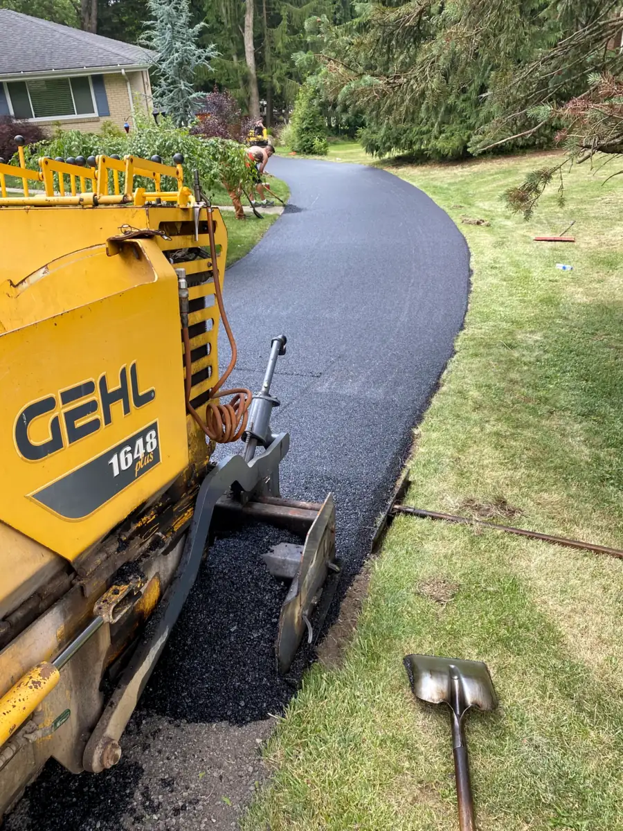 Judah Paving crew running a paver along a new curved asphalt driveway beside a lawn